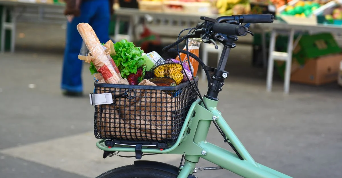 Un vélo électrique avec un panier rempli de courses sur un marché en plein air animé en France.
