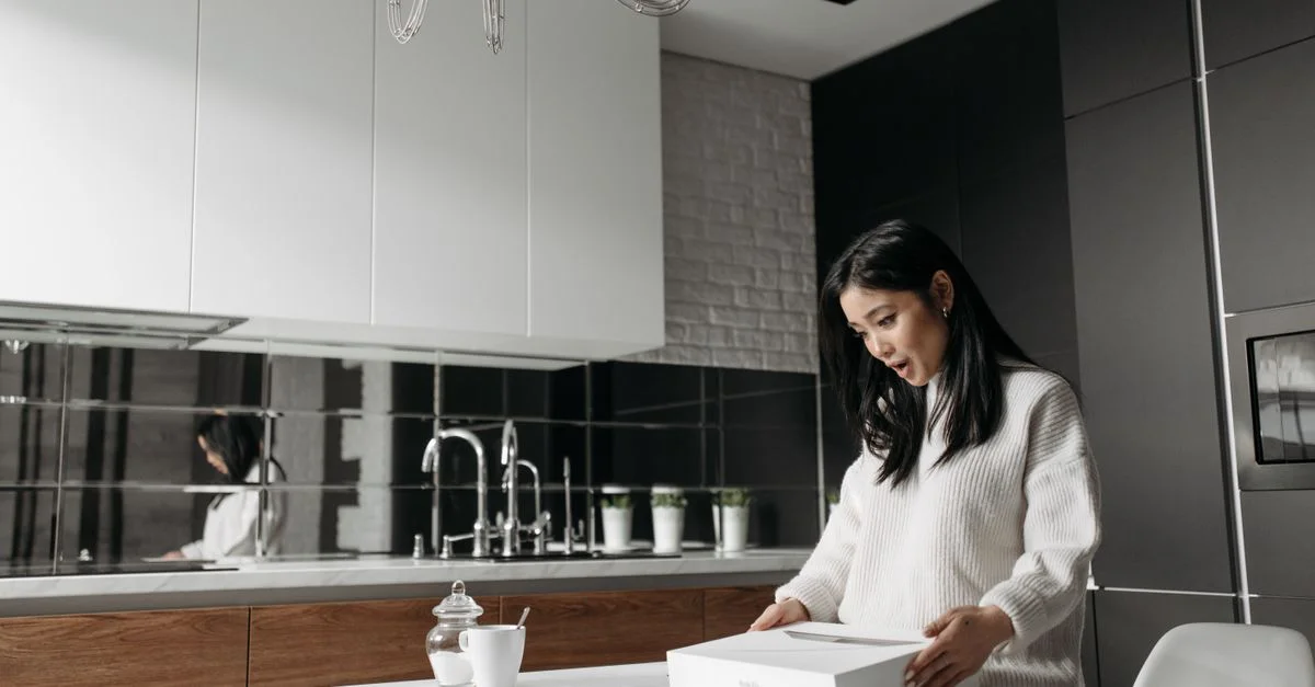Femme asiatique en pull en tricot intriguée par le contenu du colis sur la table de cuisine.