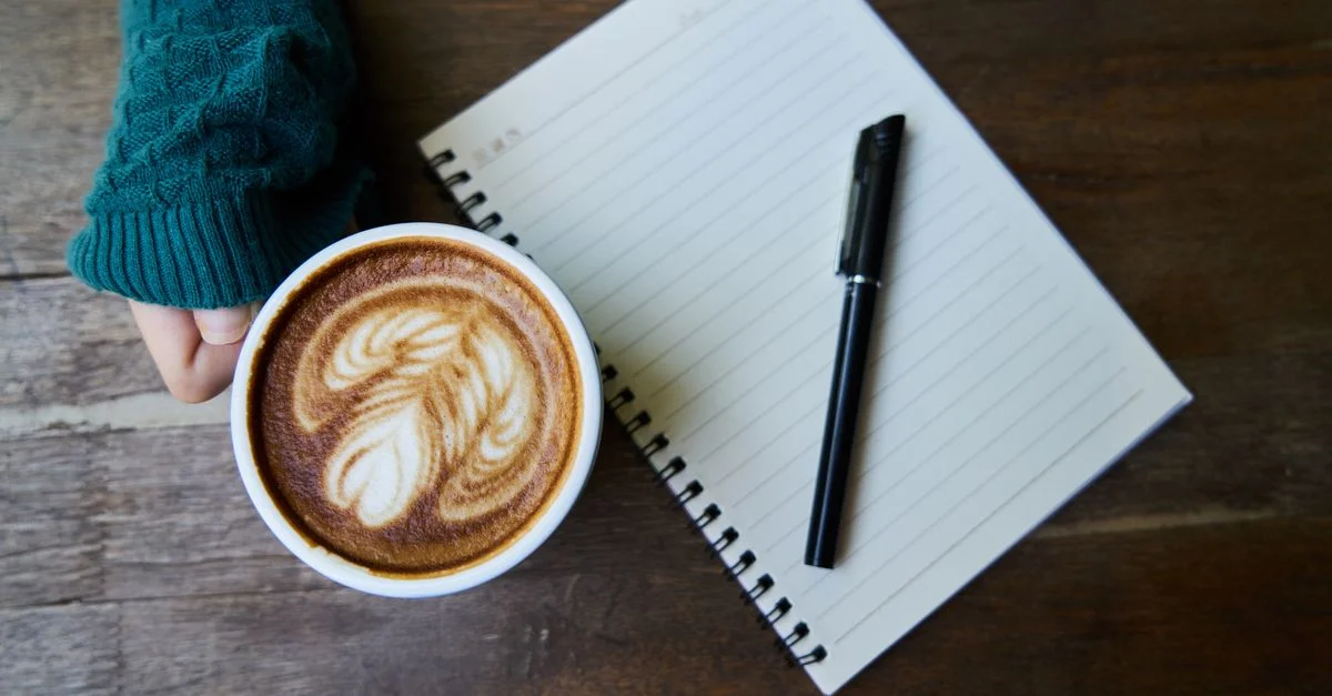 Une scène de café confortable avec un latte artistiquement préparé, à côté d'un carnet sur une table en bois.