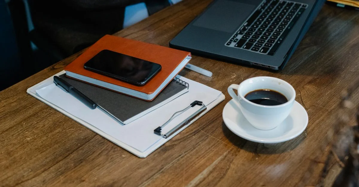 Un espace de travail moderne avec un ordinateur portable, une tasse de café et des carnets sur un bureau en bois.
