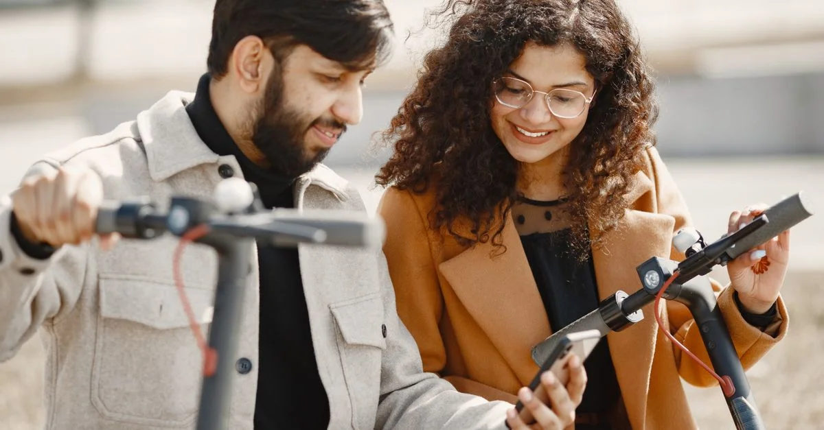 Un couple joyeux explore le plein air avec des trottinettes électriques tout en utilisant un smartphone.